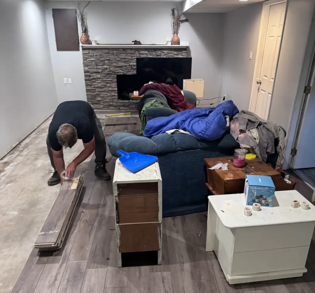 Man working on basement flooring with furniture and household items gathered during a basement cleanout