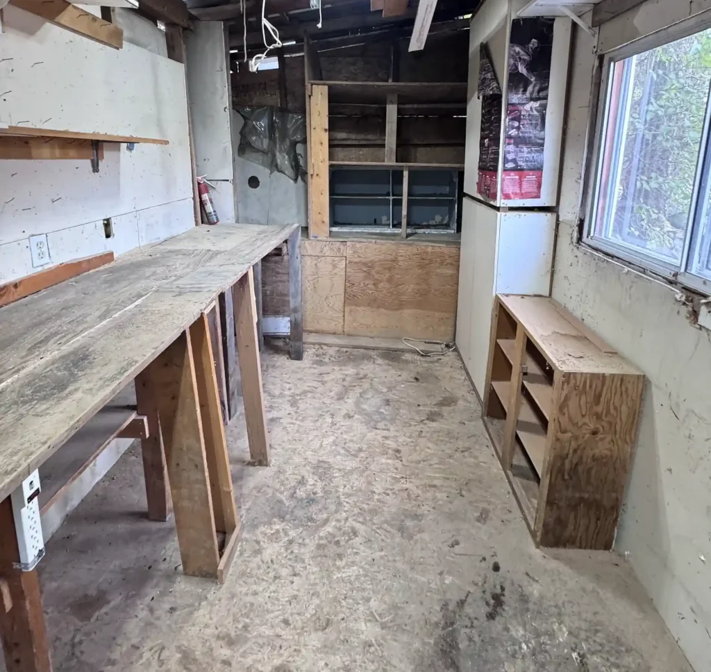 Cleared wooden workshop interior with empty workbenches, shelves, and open floor space.