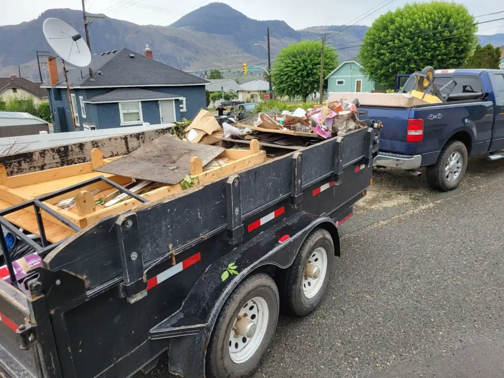 Pickup truck and trailer loaded with wood, furniture pieces, and mixed property cleanup debris